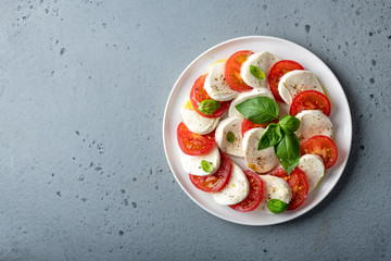 Italian caprese salad with sliced tomatoes, mozzarella, basil, olive oil on a blue background. Top view, place for text.