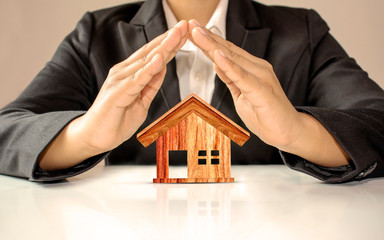 The model of a brown wooden house with the hands of a businessman surrounds the concept of investing in real estate and saving money on home purchases.