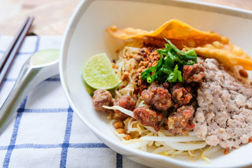 Close up shot selective focus of Thai traditional noodle with pork, meatball and fried wonton with wood chopstick and spoon. Tasty spicy local food.