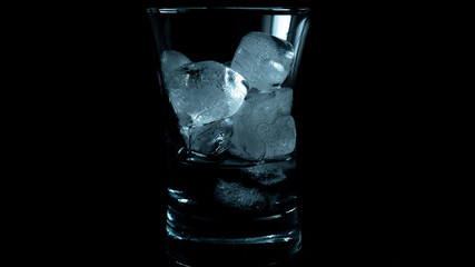 Close-up of melting blue ice cubes in glass with black background