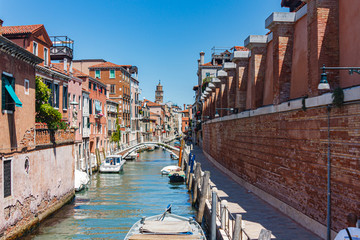 Fototapeta na wymiar View of one of the canals with a bridge and a street of Venice, built up with red brick houses. Venice, Italy, Europe.