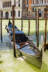 Fototapeta na wymiar Venetian gondola at the pier between the wooden poles on the Grand Canal on a sunny summer day, Venice, Italy