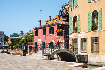 Fototapeta na wymiar Brightly colored old buildings connected to the street by a picturesque bridge thrown across a small canal in Venice, Italy