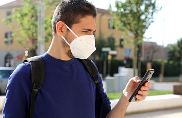 COVID-19 Mobile Application Young Man Wearing KN95 FFP2 Mask Using Smart Phone App in City Street...