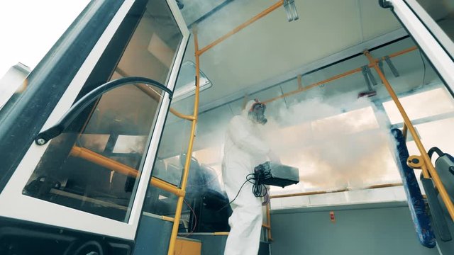 Man in hazmat sanitizes a bus to kill virus.
