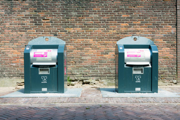 Underground recycle trash bins in front of a brick wall.