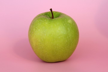 Green yellow apple on a pink background. Juicy ripe beautiful fruit.
