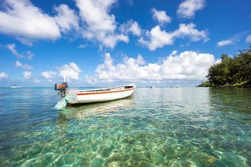 White fishing boat against the blue sky, snow-white clouds and transparent ocean water. Mauritius Island, Indian Ocean