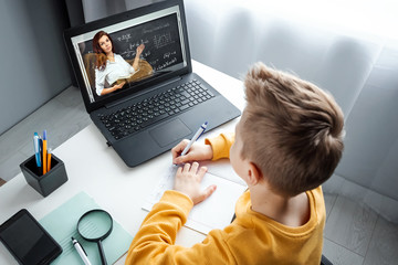 Distance learning, a boy learns math while looking at a laptop beech during an online lesson. The concept of online education, home education, technology, quarantine, self-isolation.