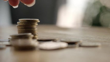 On the desk have coin pile and holding put down coin on it. Concept Planning for spending and accumulating money Including paying taxes. - Powered by Adobe