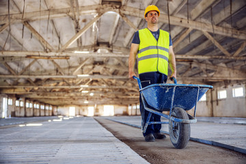 Full length of construction worker pushing wheelbarrow full of cement.