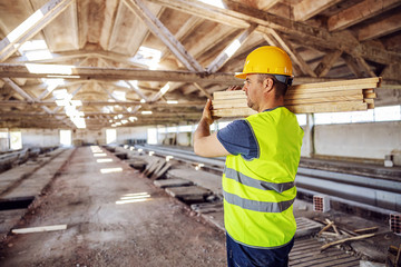 Hardworking construction worker holding joists while walking on construction site.