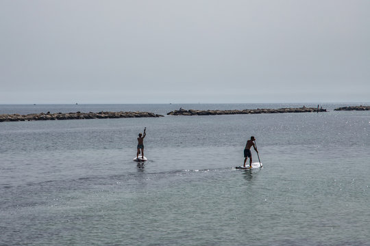 A walk through the city of Bari in the south of Italy. Two men on a surfboard do workout on the mediterranean sea.