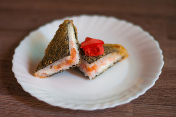 Fried sushi on a white plate with cream cheese, salmon, and ginger on wooden background.