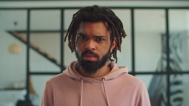 Suspicious handsome african american hipster man with dreadlocks threatening punching fist, looking with aggressive, upset expression, feeling abused and underestimated indoors.