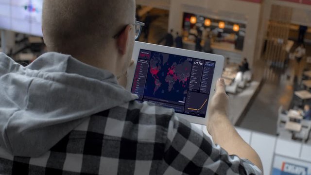 RUSSIA, St. Petersburg, may 10, 2020: 
Man with glasses sitting in shopping center and looks at the tablet map of the distribution of coronavirus. Modern technology during quarantine