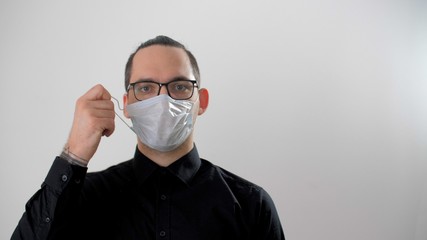 Attractive man puts on or takes off a mask. Portrait of adult european guy wearing protective medical face mask during coronavirus. Man in medical white mask. Virus prevention. Covid-19 or coronavirus