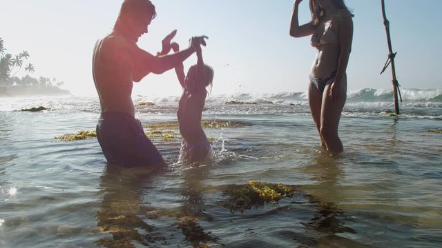 happy father bathes toddler in ocean lowering up and down enjoying holidays against amazing oceanscape slow motion. Concept parenthood tropical nature