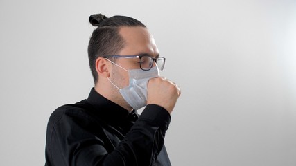 Man sneezes or coughs, covering his mouth with his hand. Portrait of a man in a white protective medical mask to prevent the spread of the virus during coronavirus or covid-19. People, healthcare.
