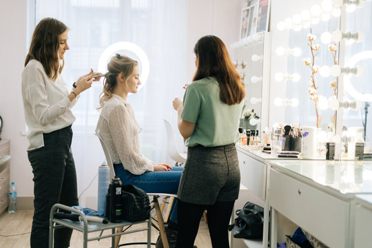 Professional female hairdresser make-up artist making hairstyle Caucasian model blonde in dressing room. Concept of backstage work.