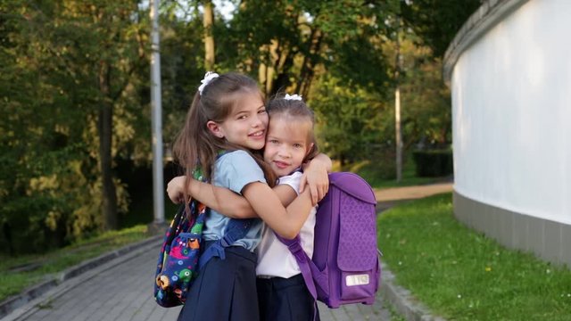 two little schoolgirls in uniform, with backpacks hugging and rejoicing after the holidays, concept back to school and September 1 - Powered by Adobe