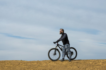 Fototapeta na wymiar Sports brutal bearded guy on a modern mountain bike. Beautiful view from the mountain. Panoramic view for banner.