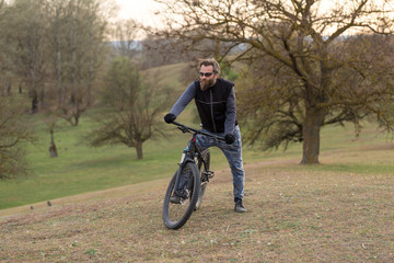 Fototapeta premium Sports brutal bearded guy on a modern mountain bike. Cyclist on the green hills in the spring.