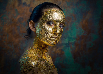 Girl with a mask on her face made of gold leaf. Gloomy studio portrait of a brunette on an abstract background.