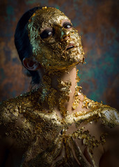 Girl with a mask on her face made of gold leaf. Gloomy studio portrait of a brunette on an abstract background.