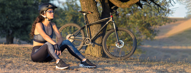 Girl on a mountain bike on offroad, beautiful portrait of a cyclist at sunset, Fitness girl rides a...