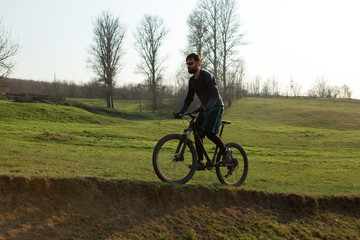 Cyclist in shorts and jersey on a modern carbon hardtail bike with an air suspension fork standing on a cliff against the background of fresh green spring forest