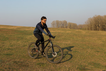 Cyclist in shorts and jersey on a modern carbon hardtail bike with an air suspension fork standing on a cliff against the background of fresh green spring forest