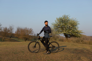 Cyclist in shorts and jersey on a modern carbon hardtail bike with an air suspension fork standing on a cliff against the background of fresh green spring forest