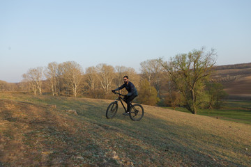 Naklejka premium Cyclist in shorts and jersey on a modern carbon hardtail bike with an air suspension fork standing on a cliff against the background of fresh green spring forest