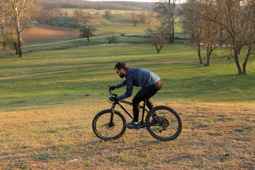 Obraz premium Cyclist in shorts and jersey on a modern carbon hardtail bike with an air suspension fork standing on a cliff against the background of fresh green spring forest