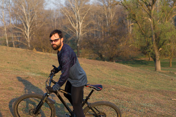 Naklejka premium Cyclist in shorts and jersey on a modern carbon hardtail bike with an air suspension fork standing on a cliff against the background of fresh green spring forest