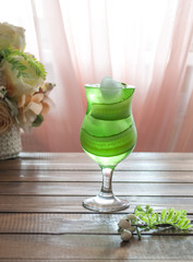 a glass of cucumber lemonade on a wooden table next to a bouquet of roses