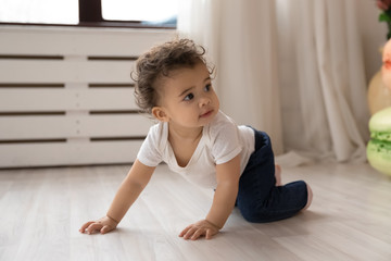 Cute little african American toddler infant go on hands and knees learn to walk on floor at home,...
