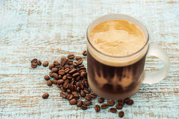 Coffee cup with milk cream foam and coffee beans, roasted grains on a vintage colored wooden background. Tasty coffee break