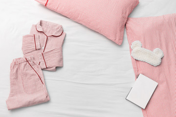 Sleepwear for slumber. Pink women pajama from cotton cloth with stripes, pillow,  fluffy sleeping eye mask and book for reading before going to bed. Top view. Flat lay.