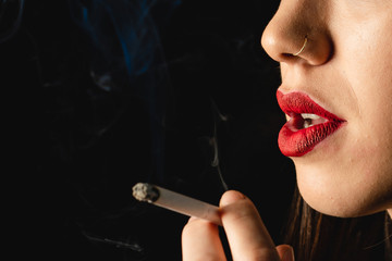 Obraz premium Low key close-up young woman smoking cigarette on black background. Copy space for text message.