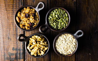 Variety of nuts, seeds and granola in a clay pots with a beautiful wooden rustic background. Healthy concept. Vegan Concept. Copy space. Top view