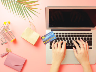 Summer shopping and online payment concept from woman hand holding pink purse with credit card and using laptop for online payment on pastel pink background. Top view