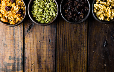 Variety of nuts, seeds and granola in a clay pots with a beautiful wooden rustic background. Healthy concept. Vegan Concept. Copy space. Top view