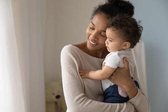 Loving african American mother hold in arms embrace little baby girl child enjoy tender family moment at home, caring young biracial mom hug cuddle cute toddler infant, childcare, maternity concept
