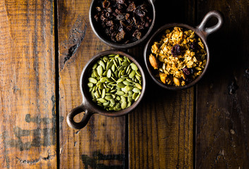 Variety of nuts, seeds and granola in a clay pots with a beautiful wooden rustic background. Healthy concept. Vegan Concept. Copy space. Top view