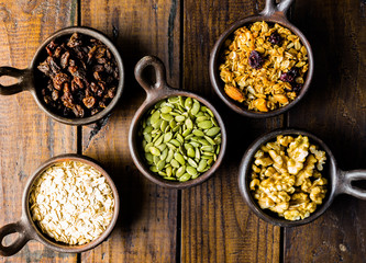 Variety of nuts, seeds and granola in a clay pots with a beautiful wooden rustic background. Healthy concept. Vegan Concept. Copy space. Top view