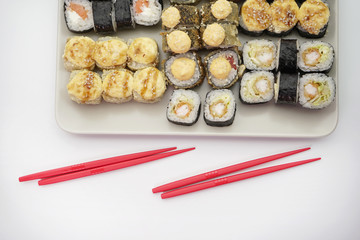 Many different delicious Japanese sushi rolls on a plate and red sticks for rolls.