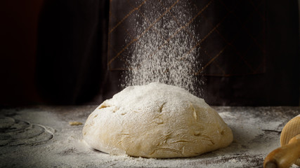 Yeast dough for a loaf of bread or other baking on the wooden table with flour.