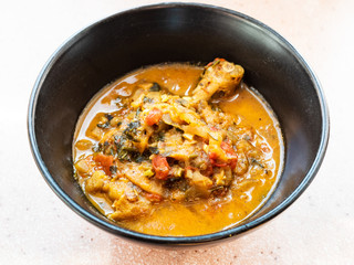 cooked Chakhokhbili (traditional georgian dish from stewed chicken, tomato, eggplant and fresh herbs) in black bowl in home kitchen